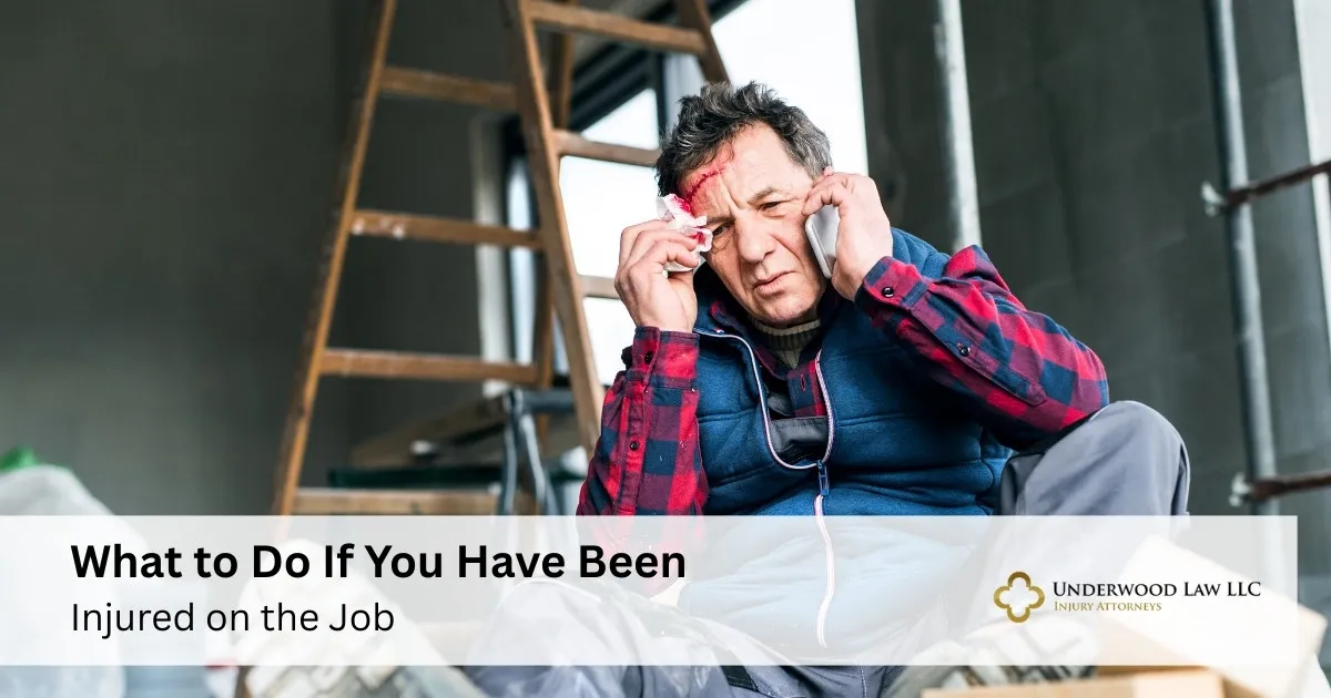 Middle-aged man with forehead injury sitting on floor, talking on phone, wooden ladder in background.