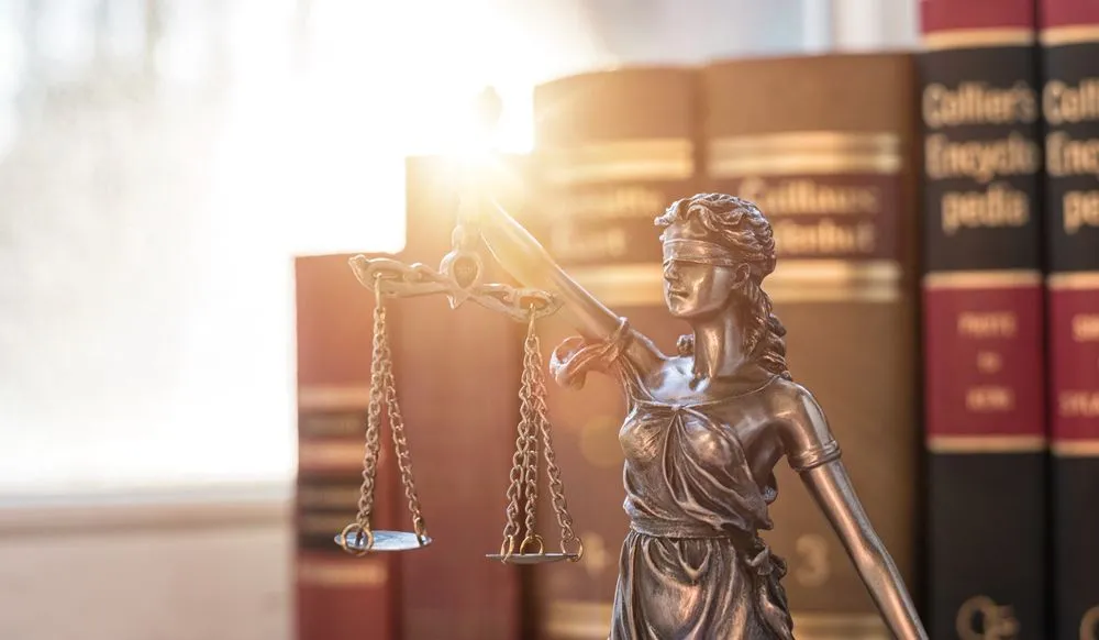 Bronze statue of Lady Justice holding scales, with legal books in background.