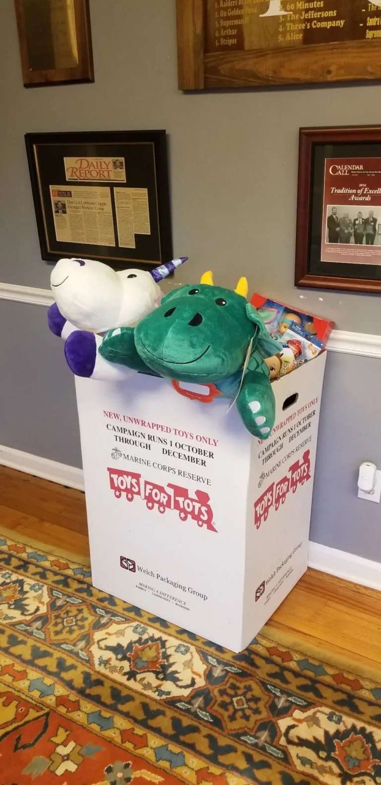 White Toys for Tots donation box filled with plush unicorn and green dragon toys.