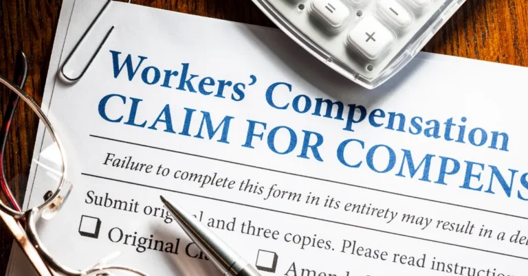 Close-up of a Workers' Compensation claim form with a pen, glasses, and calculator on a wooden desk.