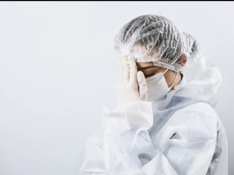 Healthcare worker in full protective gear, including mask and gloves, appearing stressed.