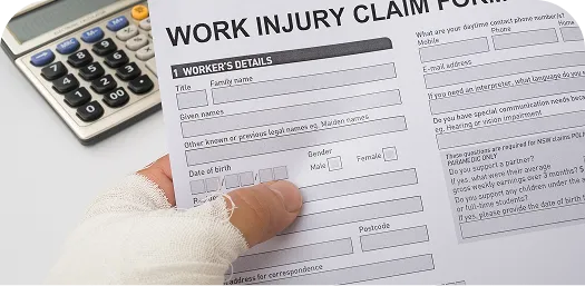 Hand with bandaged thumb holding a work injury claim form next to a calculator.