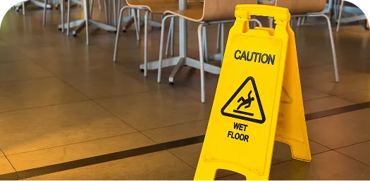 Yellow caution sign on tiled floor with "Caution Wet Floor" warning near chairs.