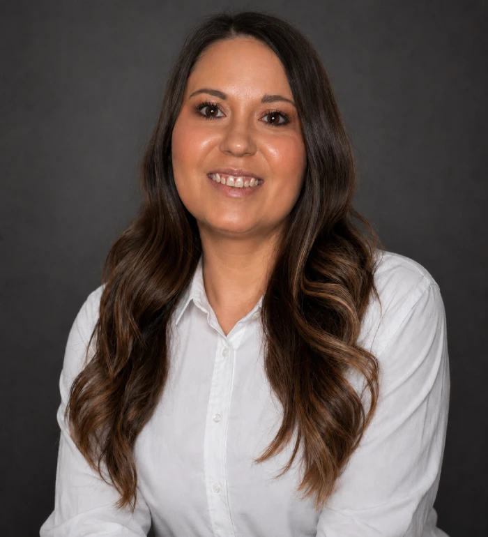 Professional portrait of a woman with long wavy brown hair wearing a white button-up shirt.