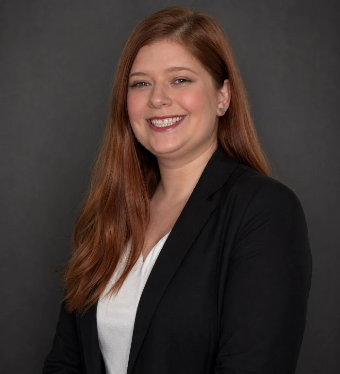 Professional portrait of a smiling woman with long red hair, wearing a black blazer and white top.