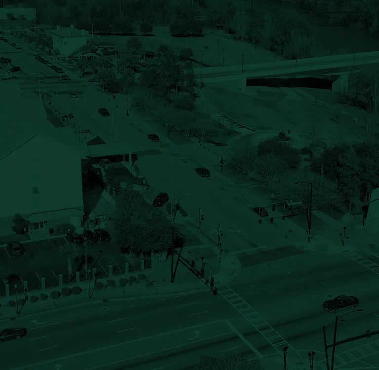 Aerial view of an urban intersection with vehicles, traffic lights, trees, and adjacent buildings.