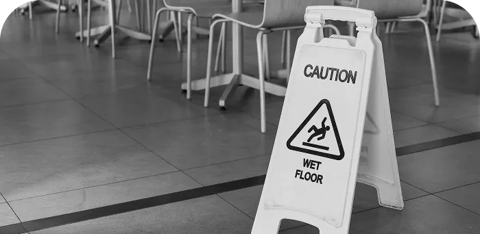 White plastic caution sign displaying "Caution Wet Floor" with a slipping figure in a tiled indoor area.