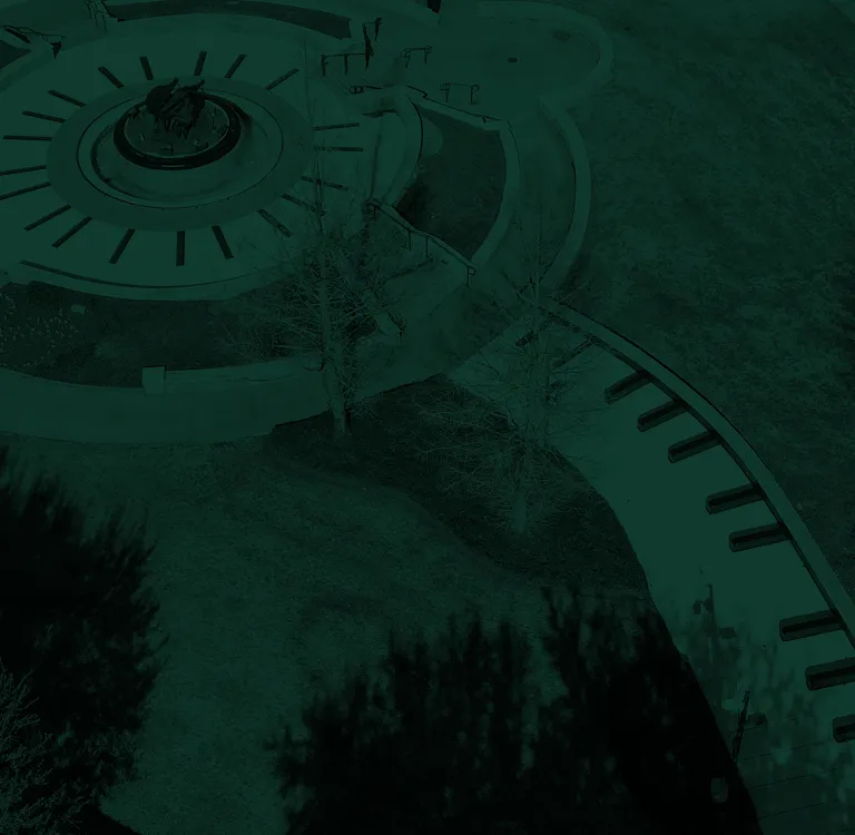 Aerial view of a circular outdoor seating area with steps and surrounding pathways in a grassy park.