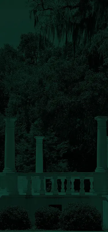 Stone balustrade with columns in front of dense green foliage and hanging moss.