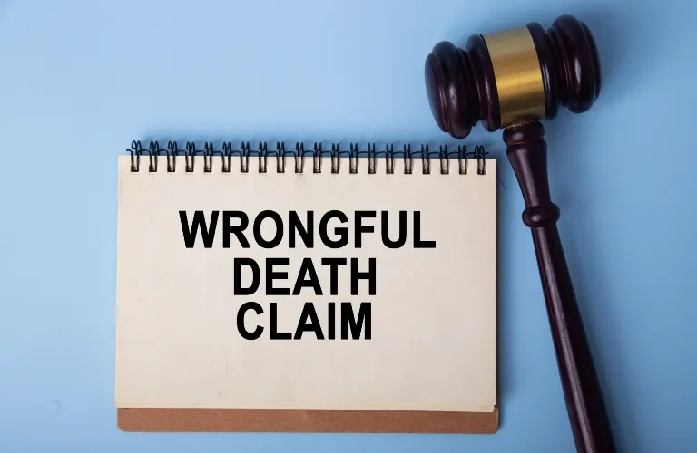 Spiral-bound notepad with "WRONGFUL DEATH CLAIM" text and wooden judge gavel on blue background.