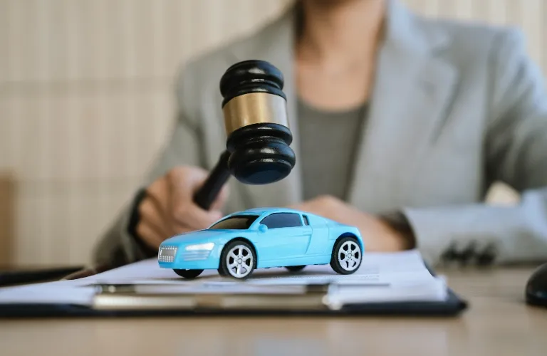 Person in gray blazer holding gavel above blue toy car on documents.
