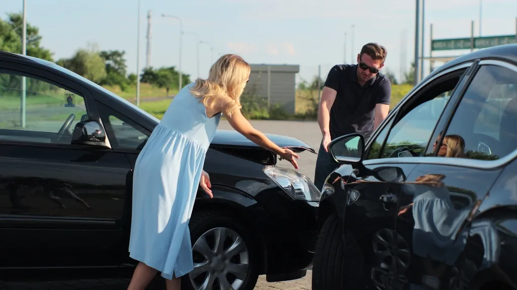Two individuals inspecting damage on the front of two black cars after a collision.