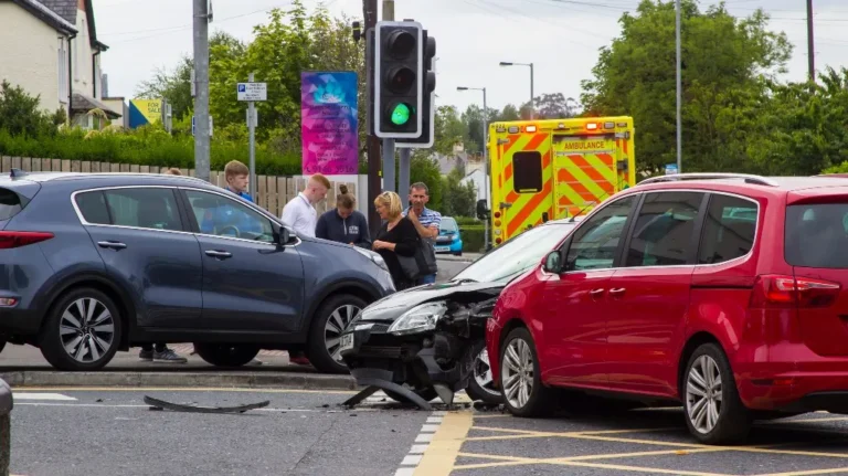 Scene of a multi-vehicle collision at an intersection with an ambulance and bystanders present.