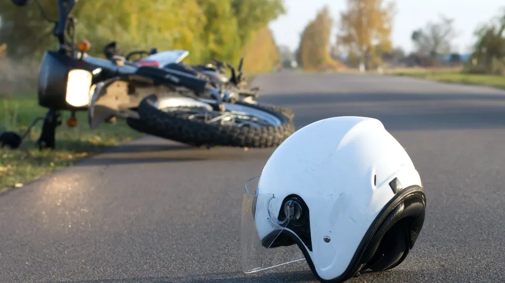 White motorcycle helmet lying on road with fallen motorcycle in the background.