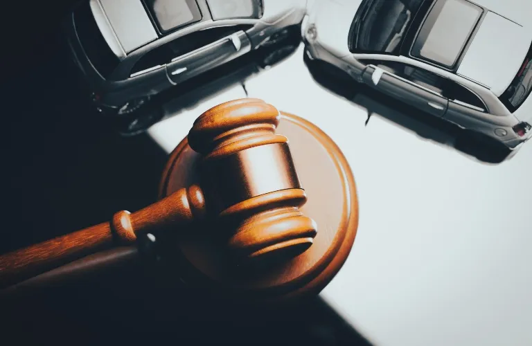 Wooden judge's gavel placed between two white toy cars on a white surface.