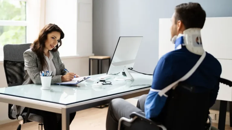 Businesswoman consulting male patient with neck brace and arm sling in modern office.
