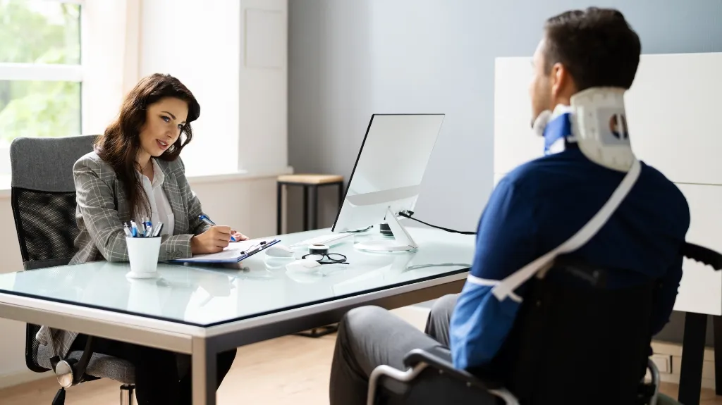 Businesswoman consulting male patient with neck brace and arm sling in modern office.