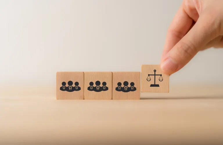 Hand placing wooden block with justice scale icon next to three blocks with businesspeople icons.