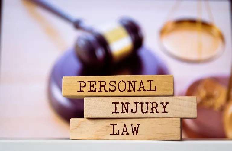 Stacked wooden blocks with the words "Personal Injury Law" in front of a blurred gavel and scales of justice.