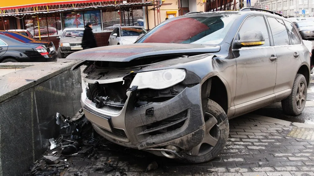 Damaged gray SUV with front-end collision parked on a city street near a sidewalk.